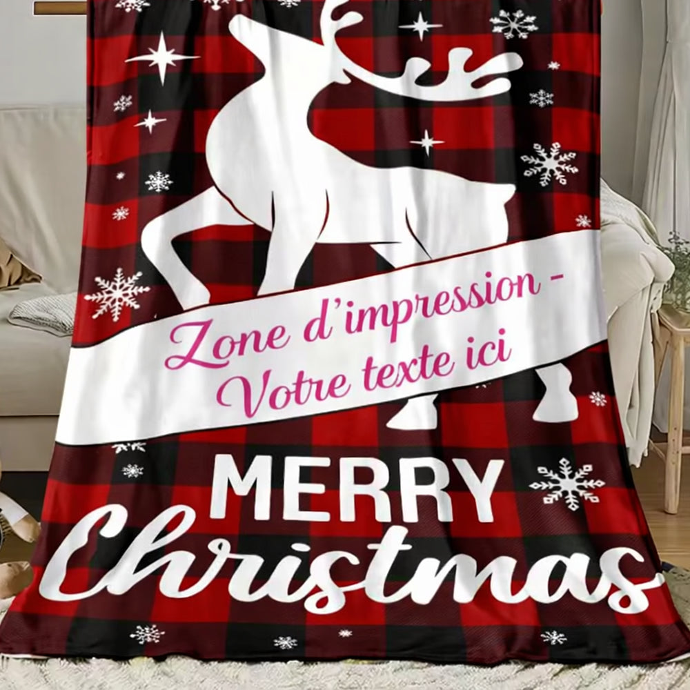 Un plaid personnalisé motif renne de noël avec grand renne blanc, flocons et espace central pour ajouter un texte, posé sur un canapé dans un salon chaleureux.