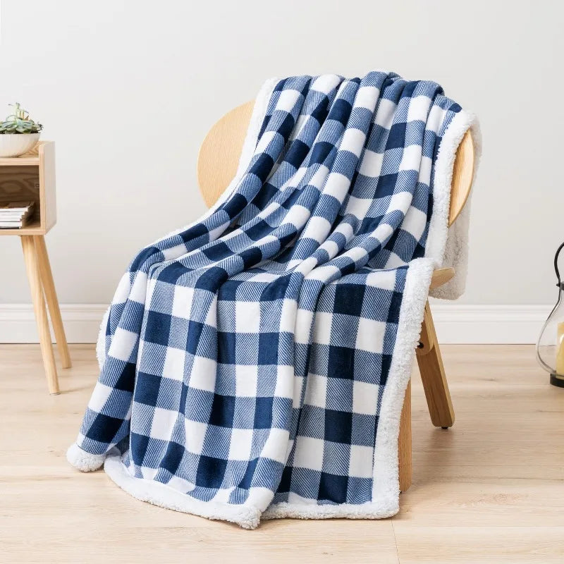 Un plaid polaire motif carreaux drapé sur un fauteuil en bois clair, avec une texture douce et moelleuse.
