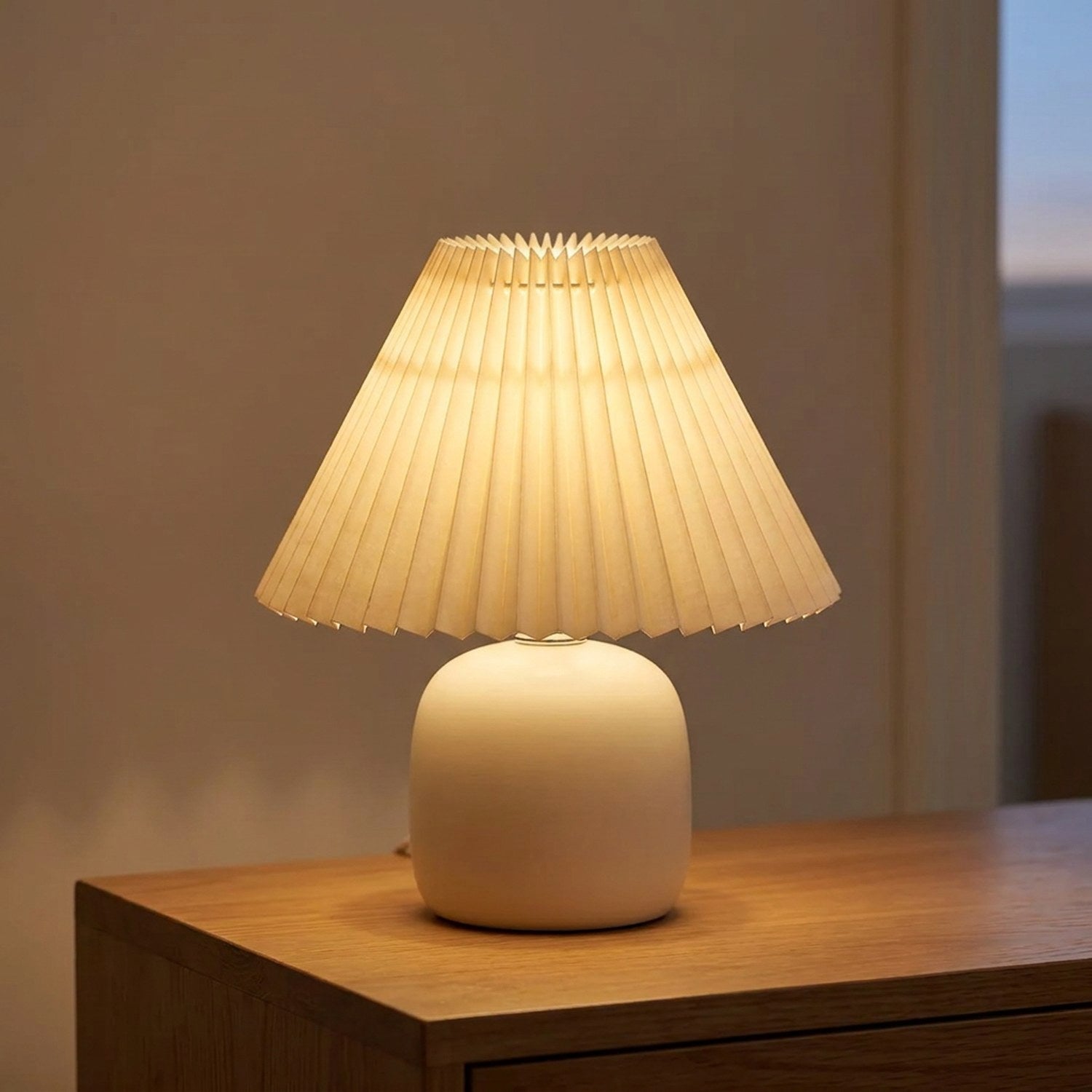Abat-jour plissé conique en tissu beige sur une lampe de table allumée dans un salon chaleureux