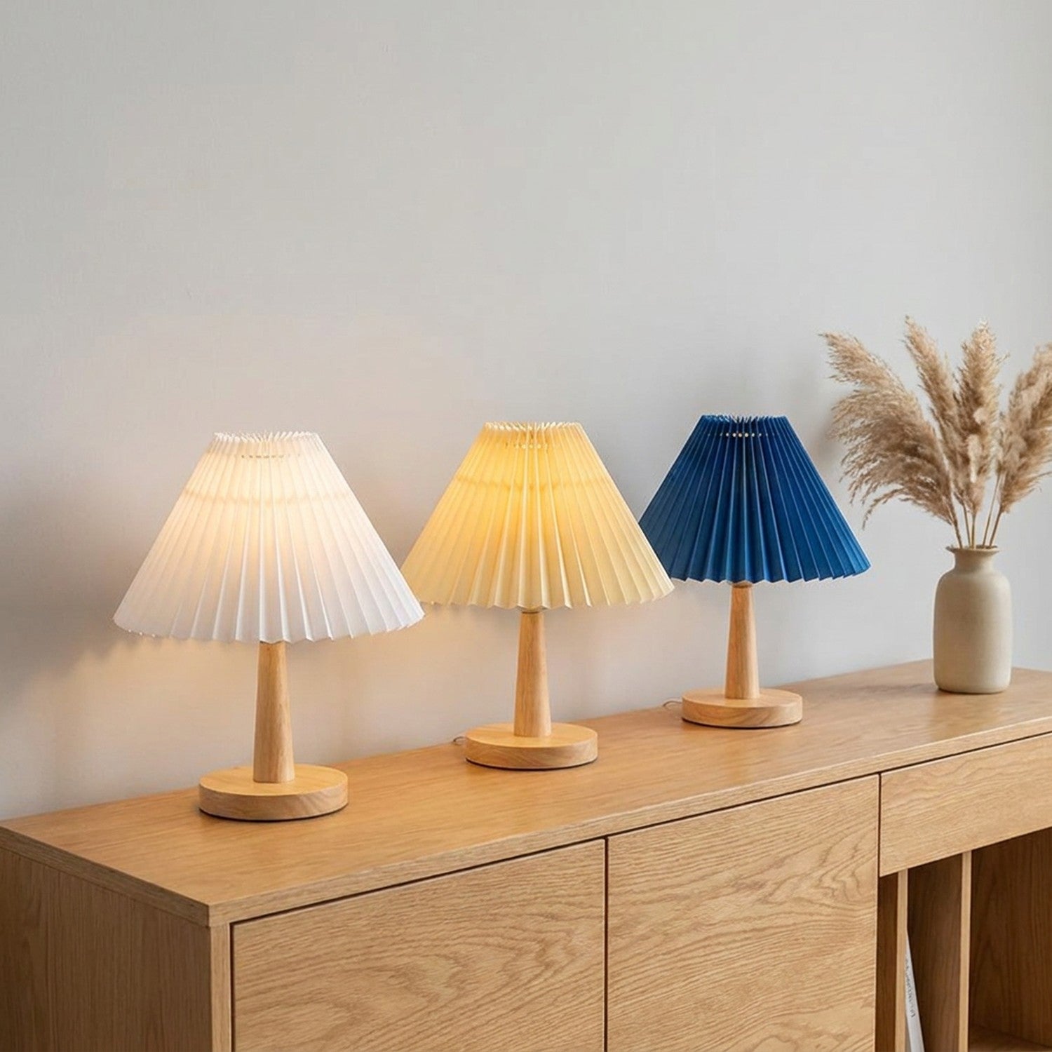 Trois abat-jours plissés de style japonais en blanc jaune et bleu sur console en bois style Japandi