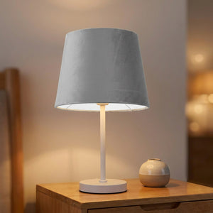 Abat-jour conique gris sur une lampe blanche posée sur une commode de chambre