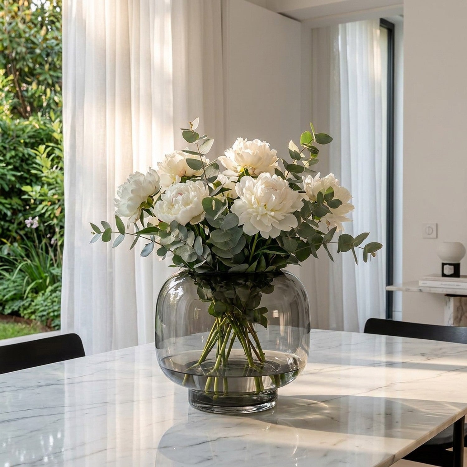 Vase bulle en verre transparent avec pivoines blanches sur table en marbre