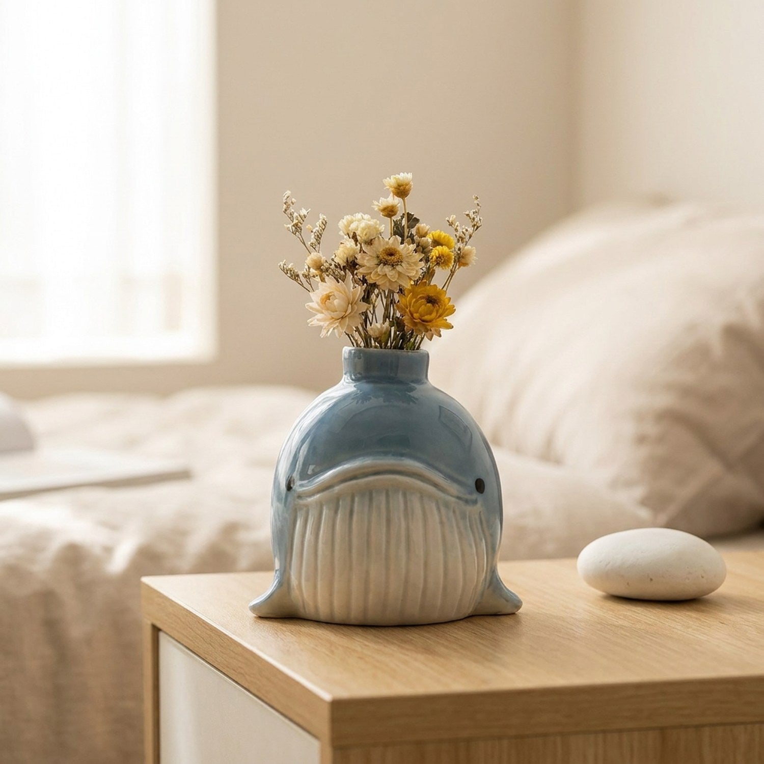 Vase baleine en céramique bleu avec fleurs séchées sur table de chevet