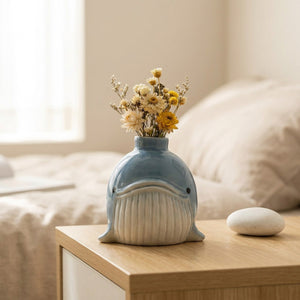 Vase baleine en céramique bleu avec fleurs séchées sur table de chevet