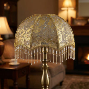 Abat-jour dome dore a franges perlees motif floral pose sur un pied de lampe en laiton dans un salon vintage chaleureux