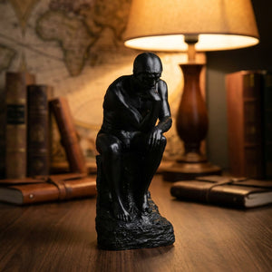 Statue penseur de Rodin noire sur bureau en noyer avec lampe dorée et livres en arrière-plan bokeh