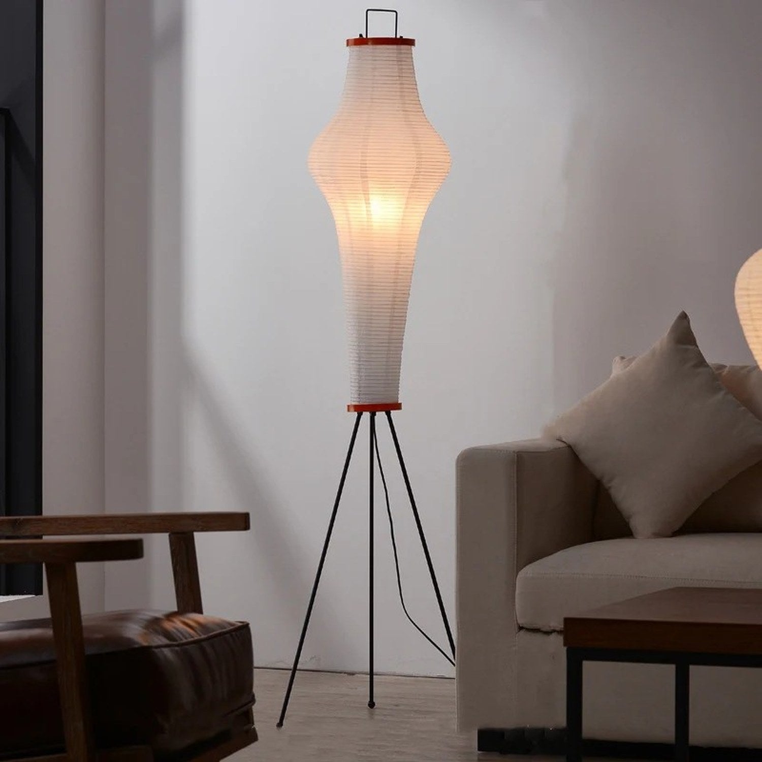Lampadaire Akari japonais allumé dans un salon avec canapé et fauteuil bois