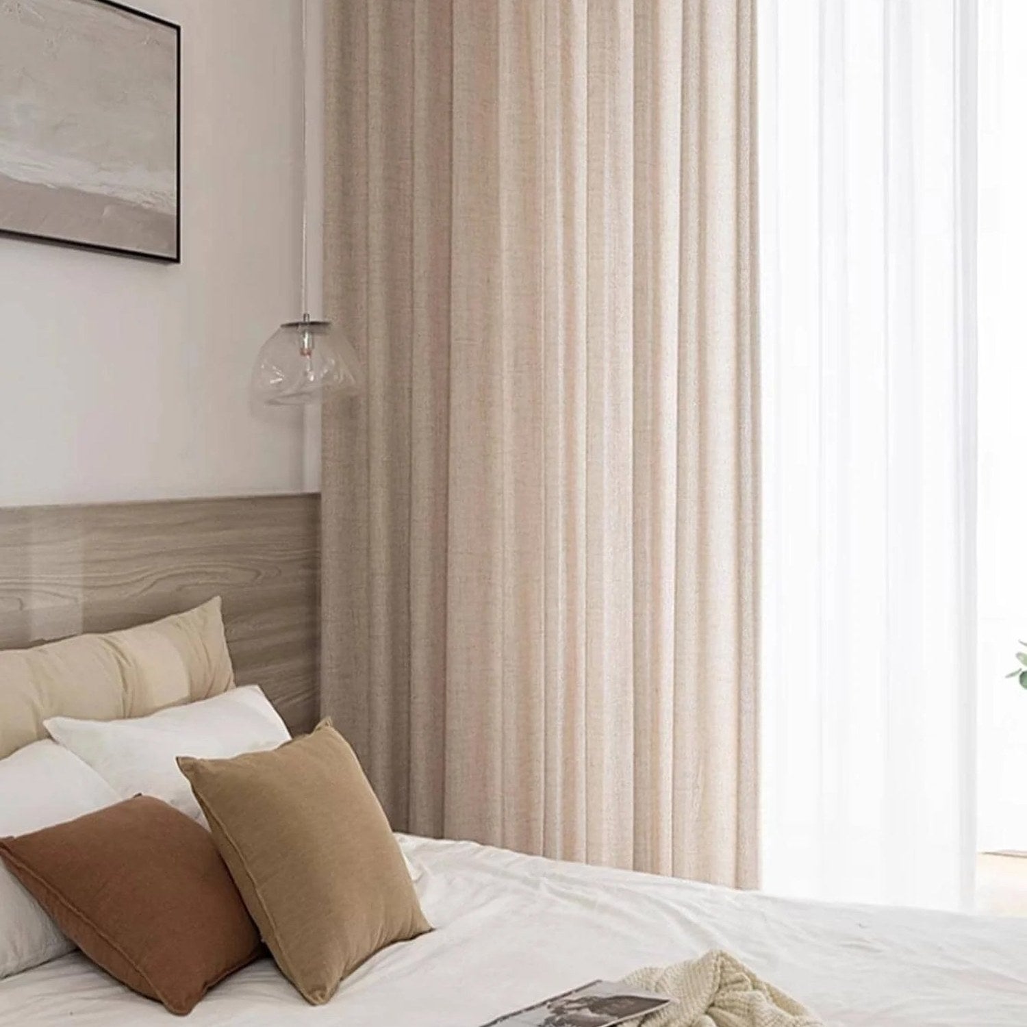 Rideau beige à œillets tombant devant une baie vitrée dans une chambre lumineuse avec lit blanc et coussins