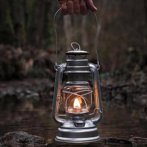 Lampe à pétrole tenue à la main allumée au bord de l'eau en forêt
