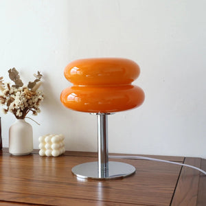 Lampe de chevet en verre forme macaron orange posée sur un meuble en bois avec un vase de fleurs séchées
