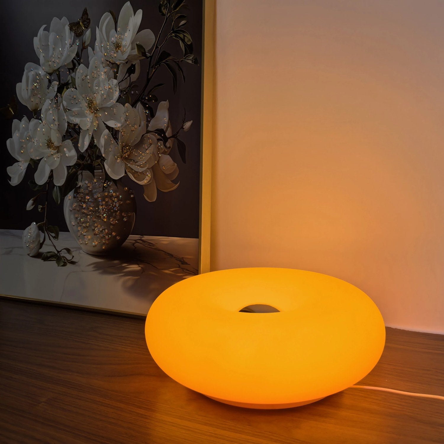 Lampe beignet Bauhaus allumée en orange sur un meuble en bois