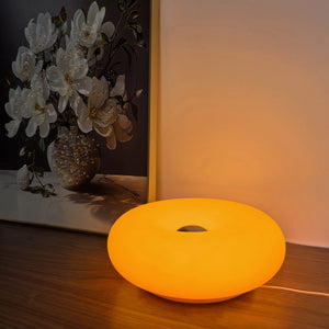 Lampe beignet Bauhaus allumée en orange sur un meuble en bois