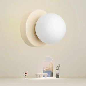 Applique murale forme boule en verre sur fond beige avec objets de décoration