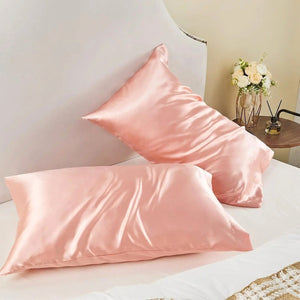 Taies d'oreiller satin roses posées sur un lit avec fleurs et table de chevet