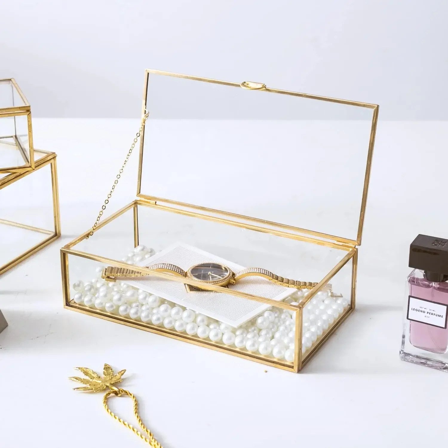 Boîte à bijoux en verre ouverte avec perles et montre sur fond blanc