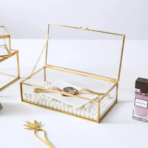 Boîte à bijoux en verre ouverte avec perles et montre sur fond blanc