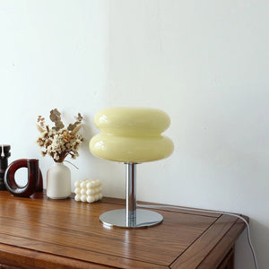 Lampe de chevet en verre forme macaron coloris jaune pâle posée sur un meuble en bois