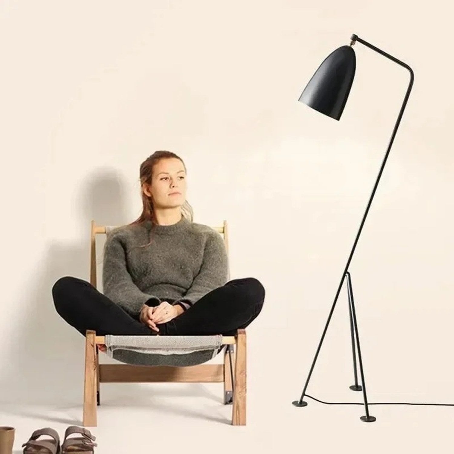 Lampadaire trépied noir à échelle réelle à côté d'une personne assise