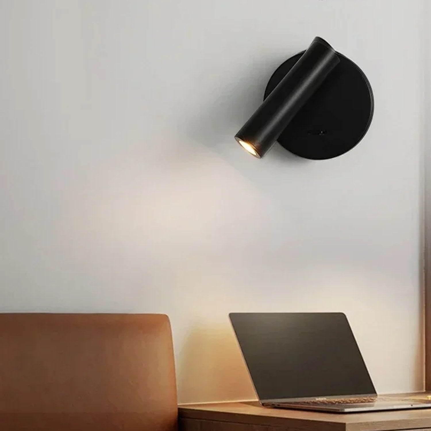 Applique murale ronde noire allumée au-dessus d'une table de chevet en bois avec un ordinateur portable