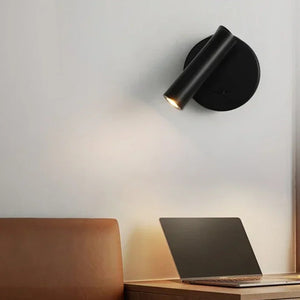 Applique murale ronde noire allumée au-dessus d'une table de chevet en bois avec un ordinateur portable