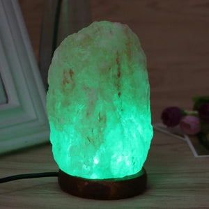 Lampe de sel de l'Himalaya allumée en vert sur une table de chevet en bois