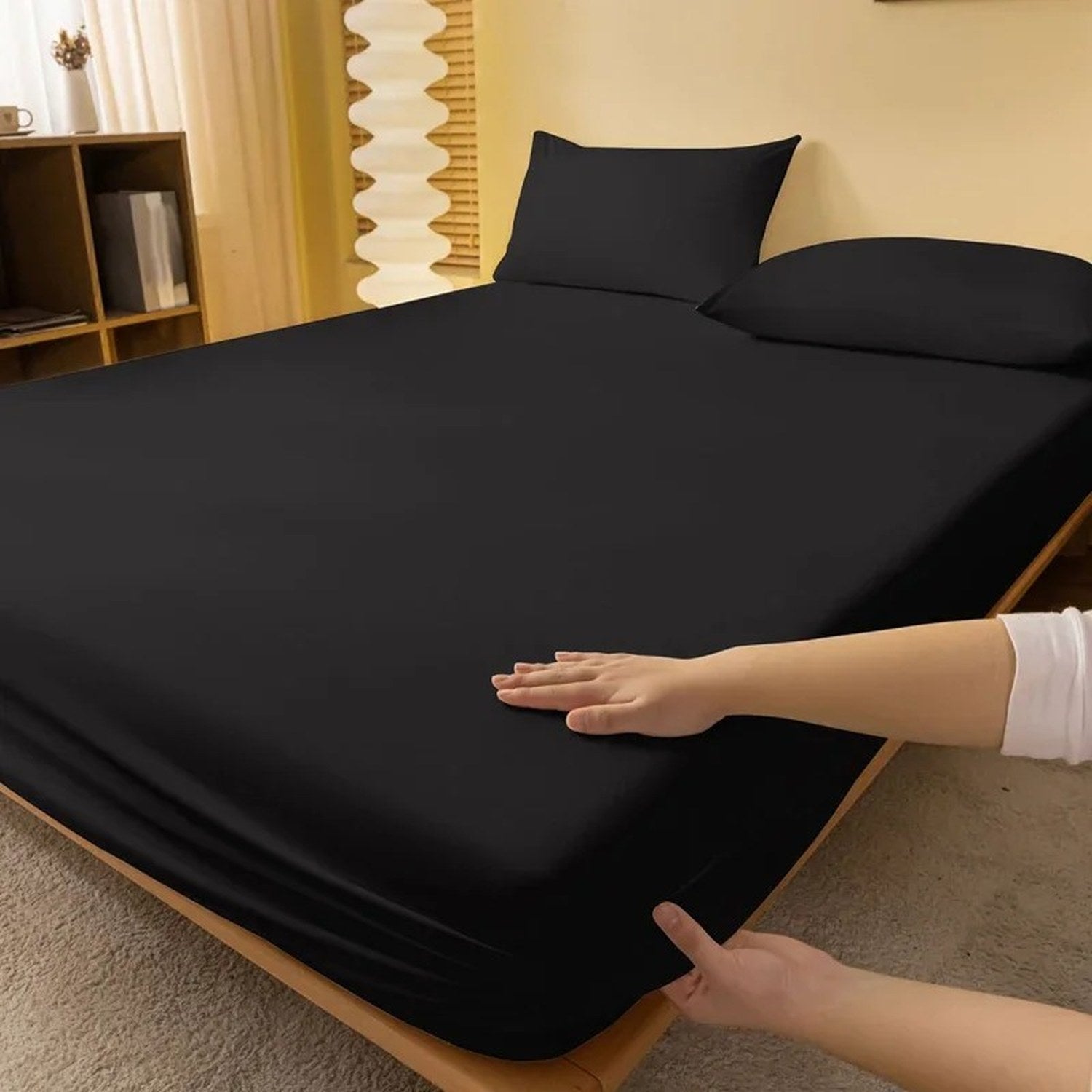 Main posée sur un drap housse noir tendu sur un matelas
