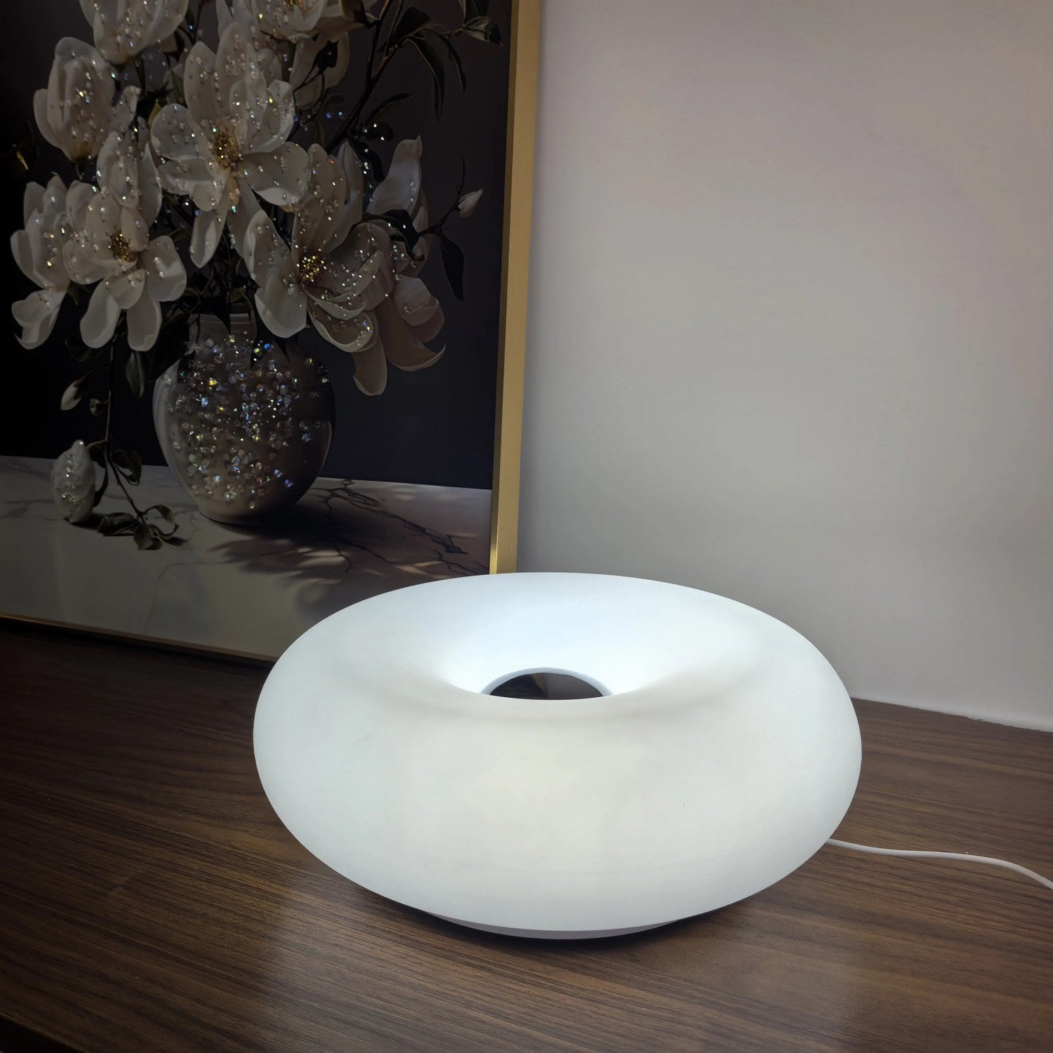 Lampe beignet Bauhaus allumée en blanc sur un meuble en bois