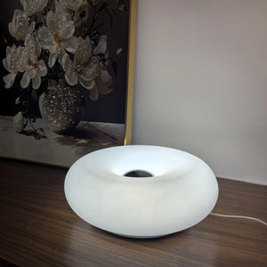 Lampe beignet Bauhaus allumée en blanc sur un meuble en bois