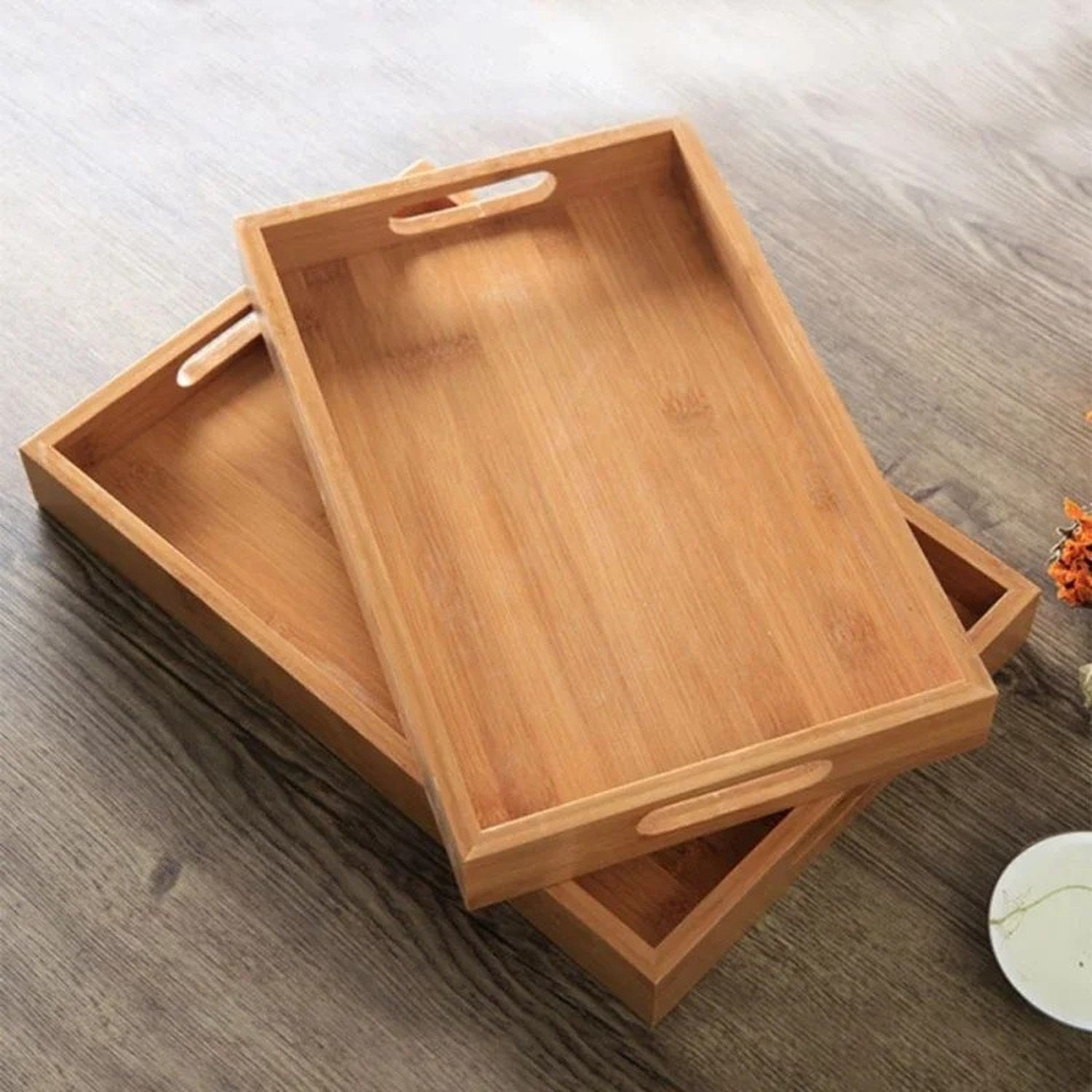 Deux plateaux en bambou empilés sur surface en bois avec fleur orange