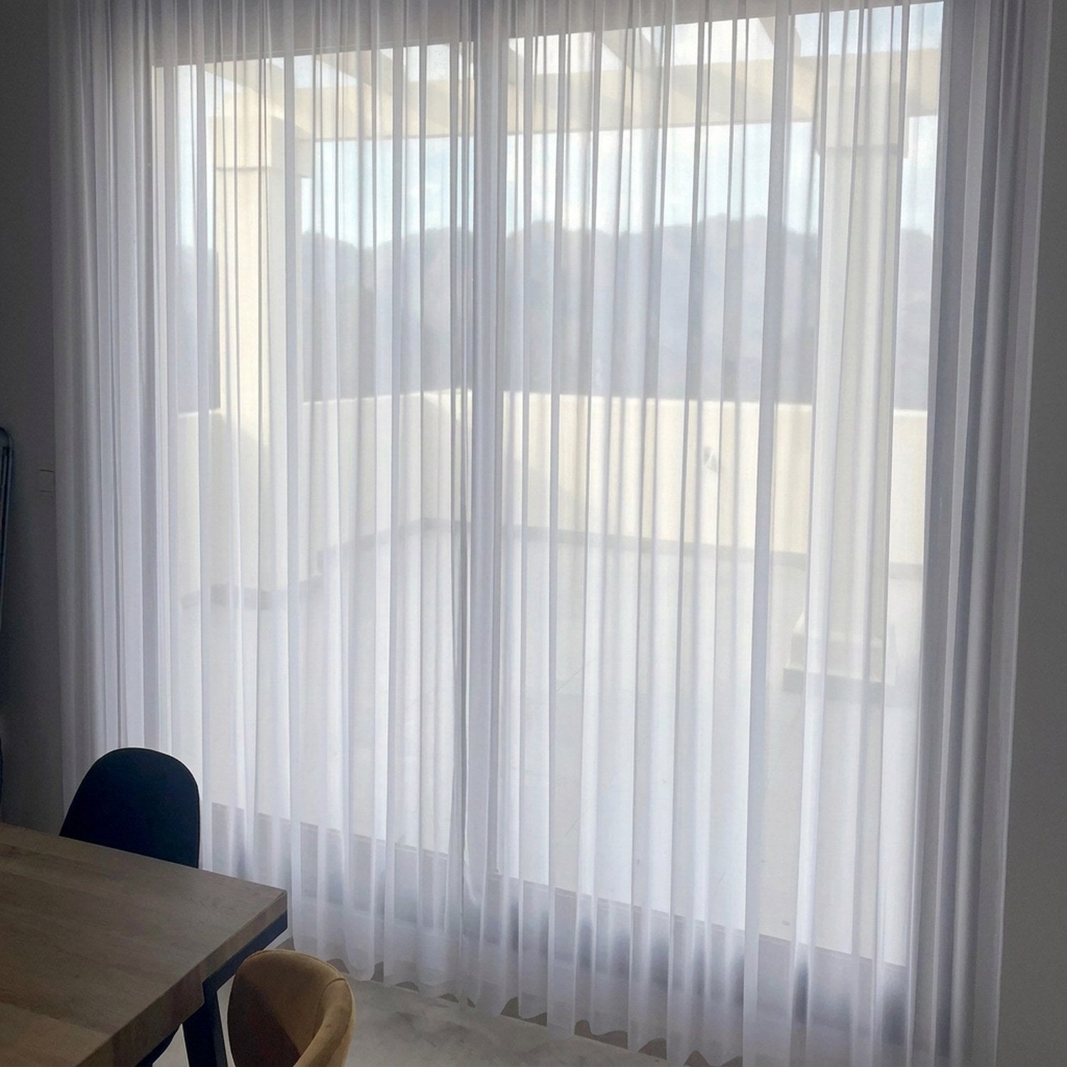 Voile blanc habillant une grande baie vitrée avec vue extérieure