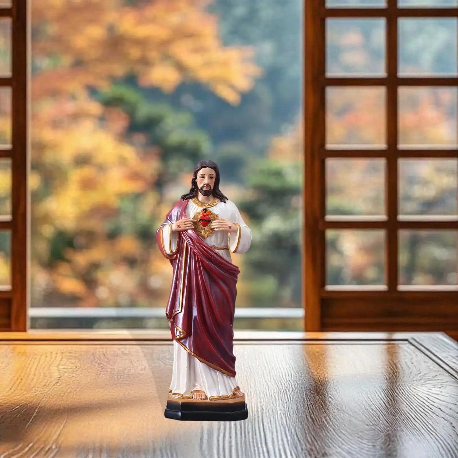 Statue Sacré-Cœur de Jésus en résine peinte sur table bois fond fenêtre automne