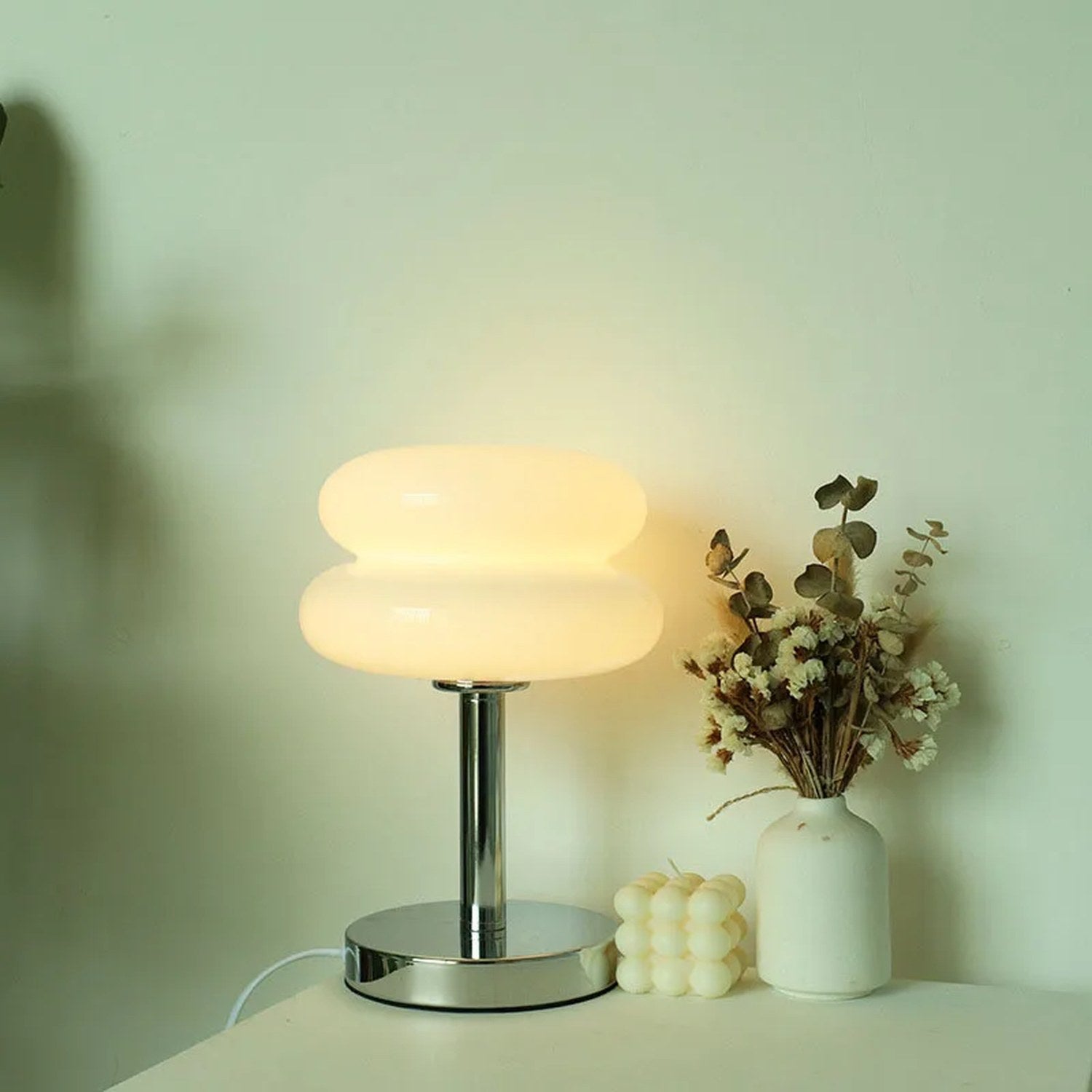 Lampe de chevet en verre forme macaron blanche allumée diffusant une lumière douce dans une chambre