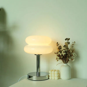 Lampe de chevet en verre forme macaron blanche allumée diffusant une lumière douce dans une chambre