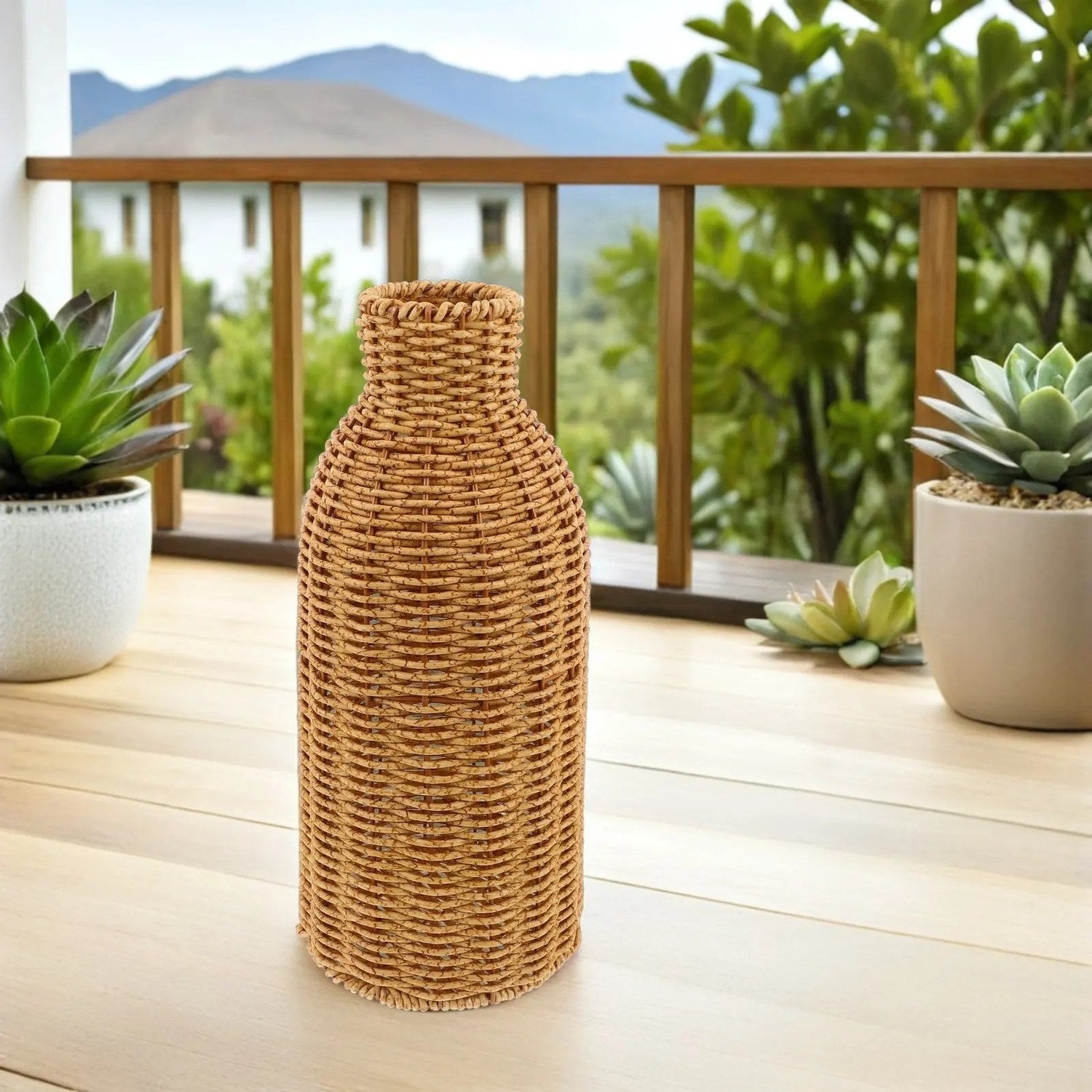 Vase en rotin tressé posé sur une terrasse en bois entouré de plantes grasses