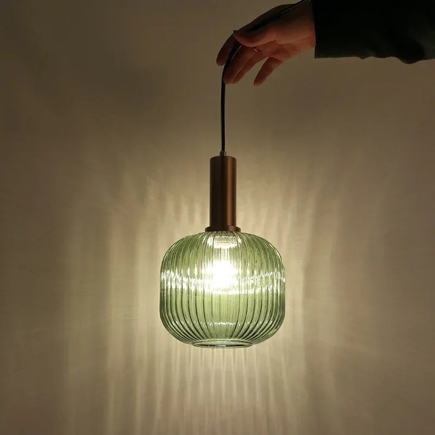 Suspension en verre vert texturé allumée dans une ambiance tamisée