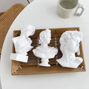 Trois bustes décoratifs en résine disposés sur un plateau en bambou sur table blanche