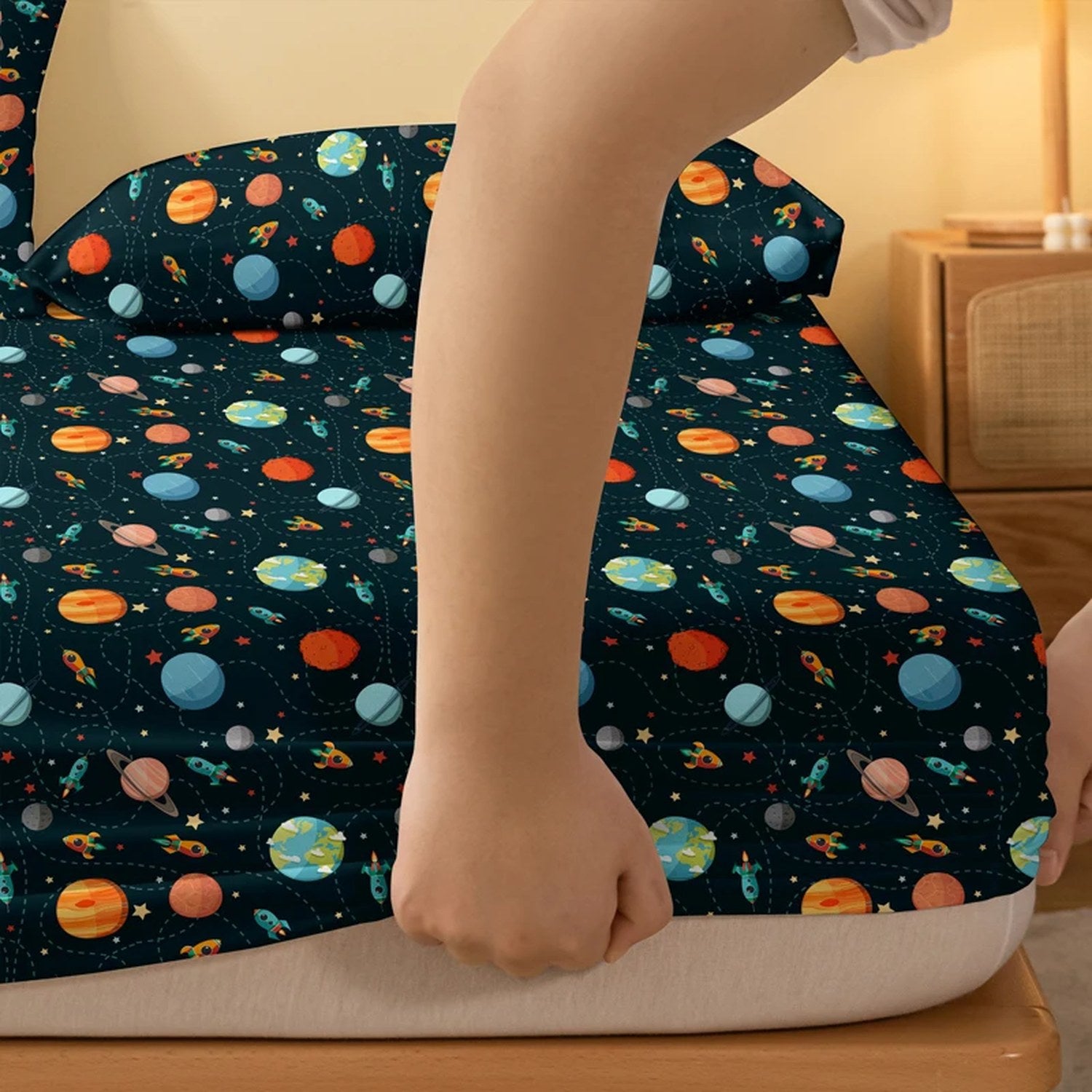 Détail du drap housse cosmos tendu sur le matelas avec motif fusées et planètes