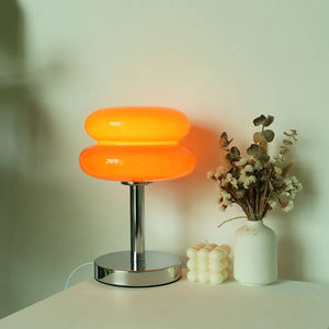 Lampe de chevet en verre forme macaron orange allumée avec un halo de lumière chaude