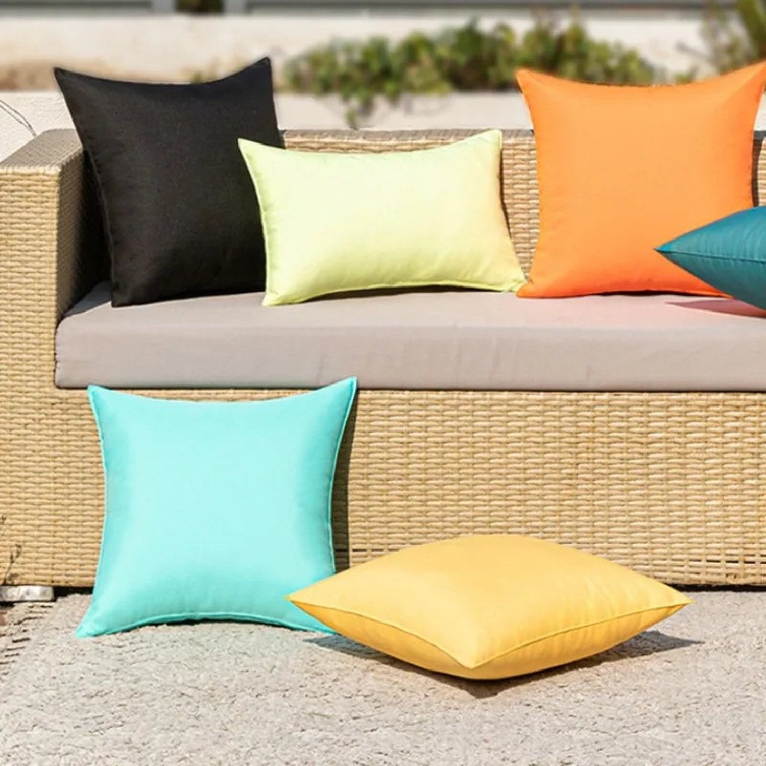 Housses de coussin extérieur noire jaune pâle et orange sur un canapé en rotin en terrasse