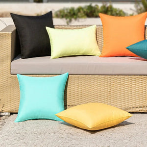 Housses de coussin extérieur noire jaune pâle et orange sur un canapé en rotin en terrasse