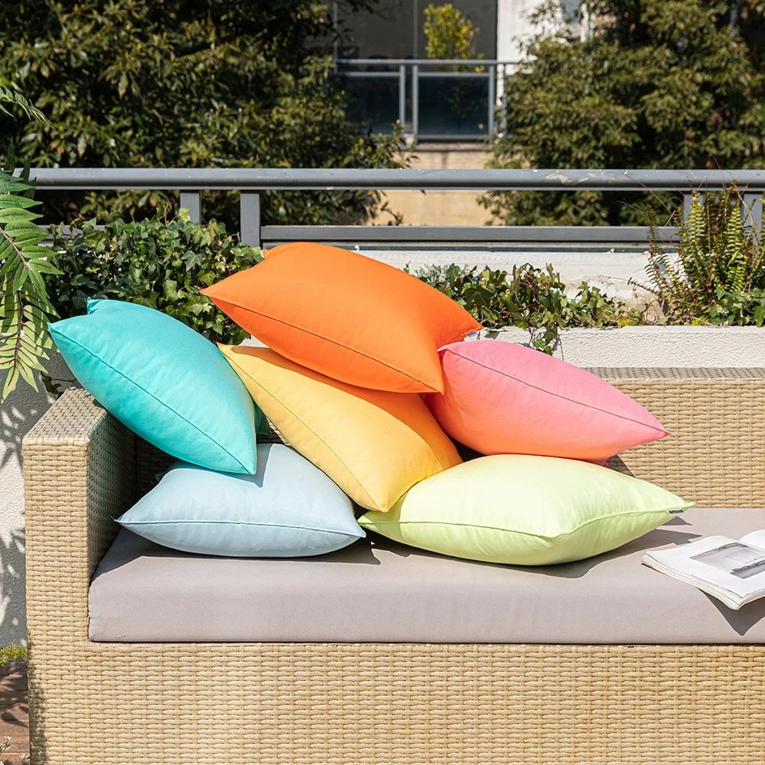 Housses de coussin extérieur turquoise et jaune posées au sol devant un canapé en rotin