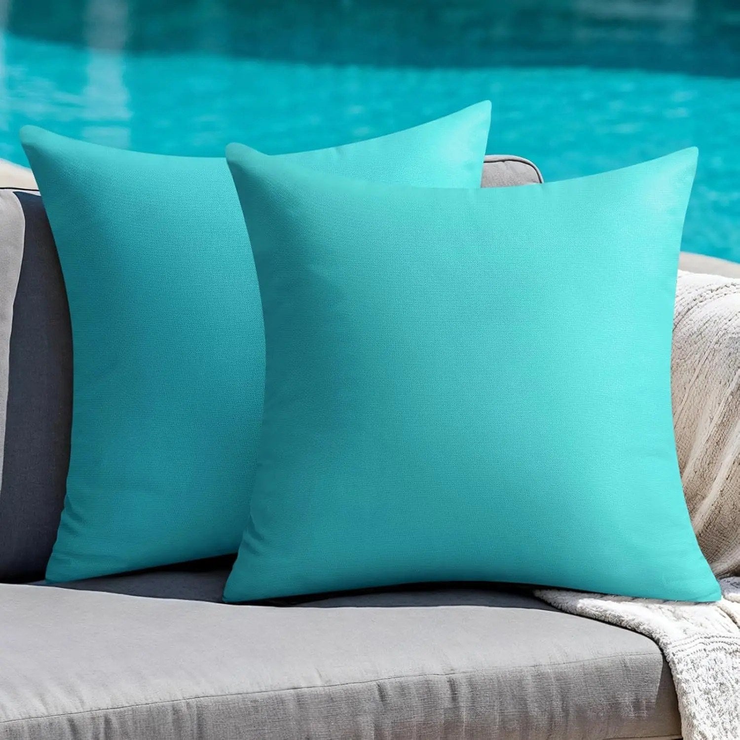 Housses de coussin extérieur turquoise posées sur un canapé de jardin gris au bord d'une piscine