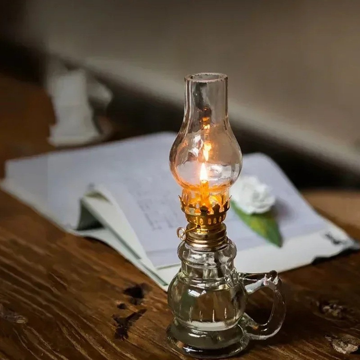Lampe à pétrole allumée posée sur un bureau en bois avec un livre ouvert