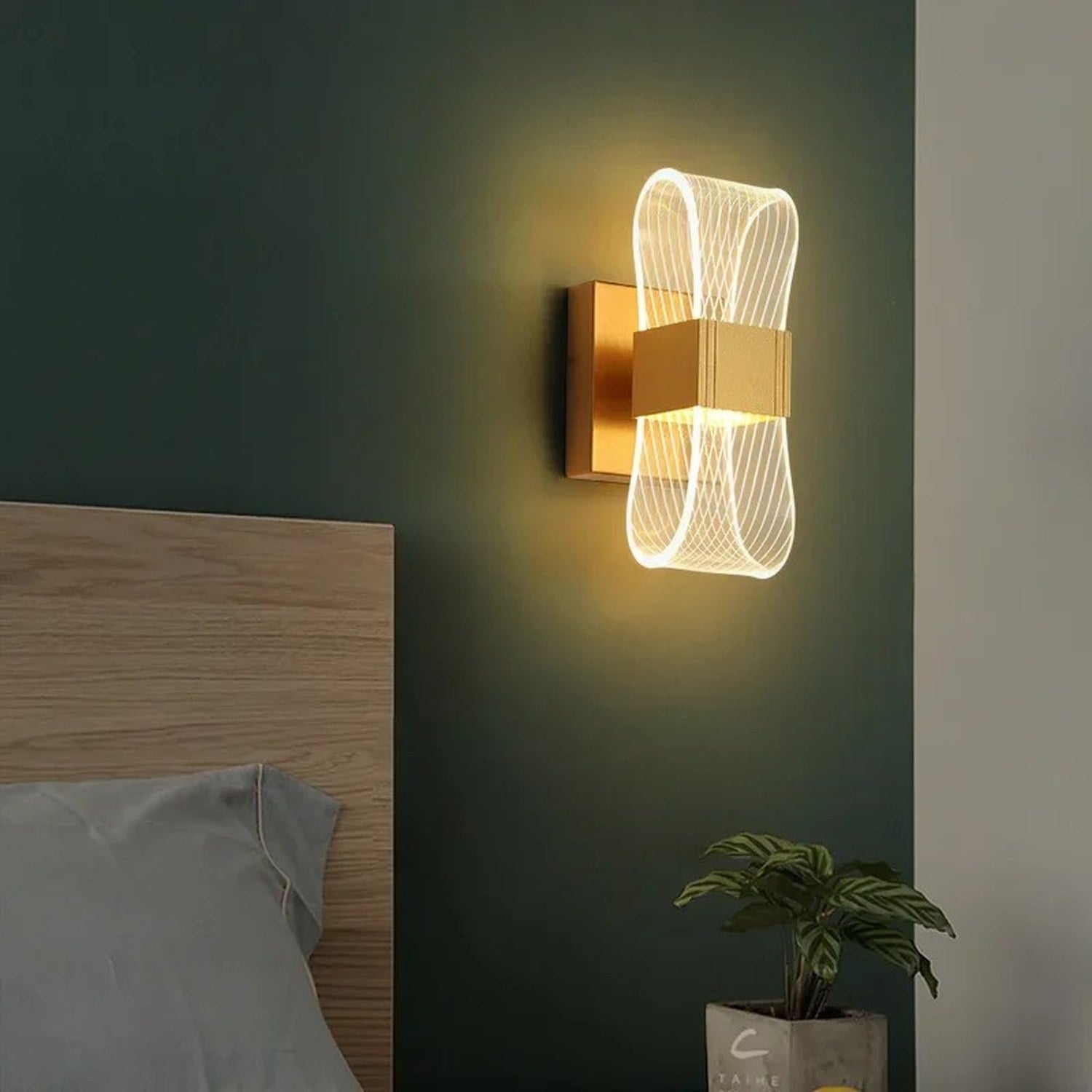 Applique murale dorée installée dans une chambre avec plante verte et tête de lit bois