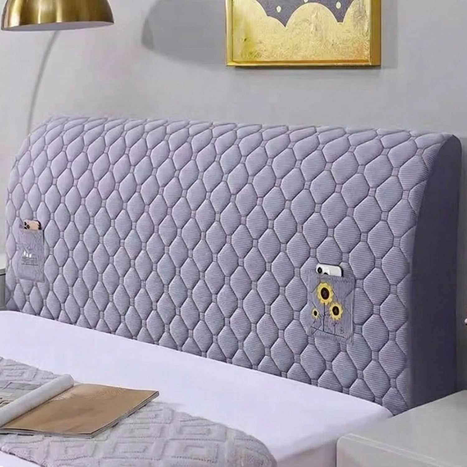 Housse de tête de lit matelassée grise installée sur un lit avec lampe de chevet dorée
