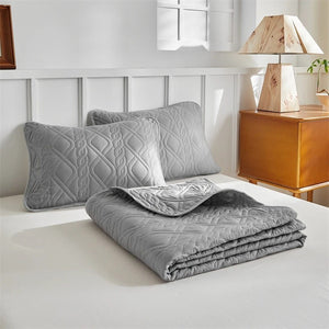 Ensemble 3 pièces gris avec taies d'oreiller pliées sur un lit