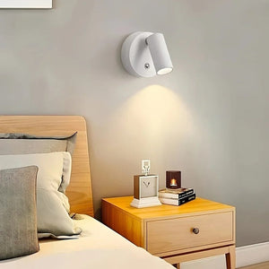 Applique murale LED blanche allumée au-dessus d'une table de chevet avec horloge et bougie