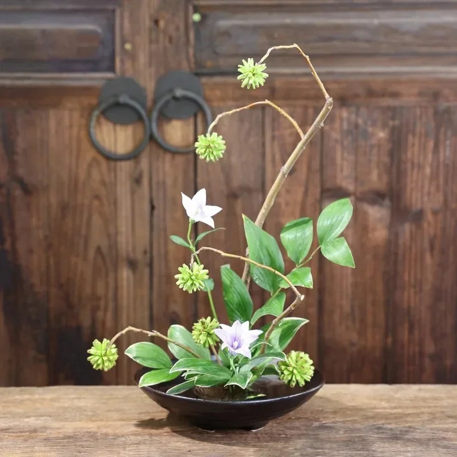 Vase japonais en céramique noire garni d'une composition florale sur socle en bois