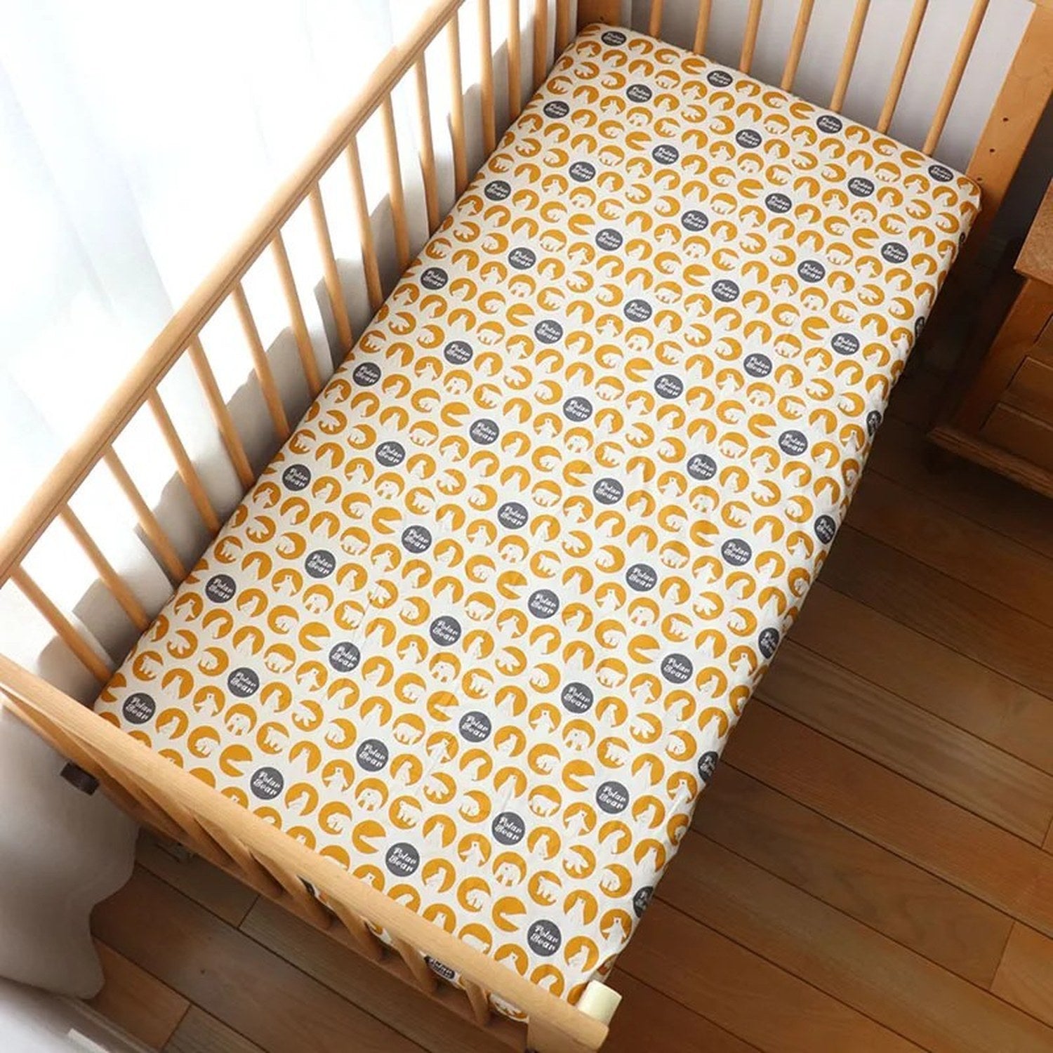 Drap housse bébé motif ourson polaire sur fond moutarde installé sur un matelas de berceau