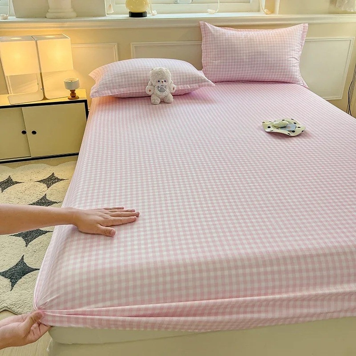Main tirant le coin elastique du drap housse a carreaux vichy rose pour montrer l ajustement